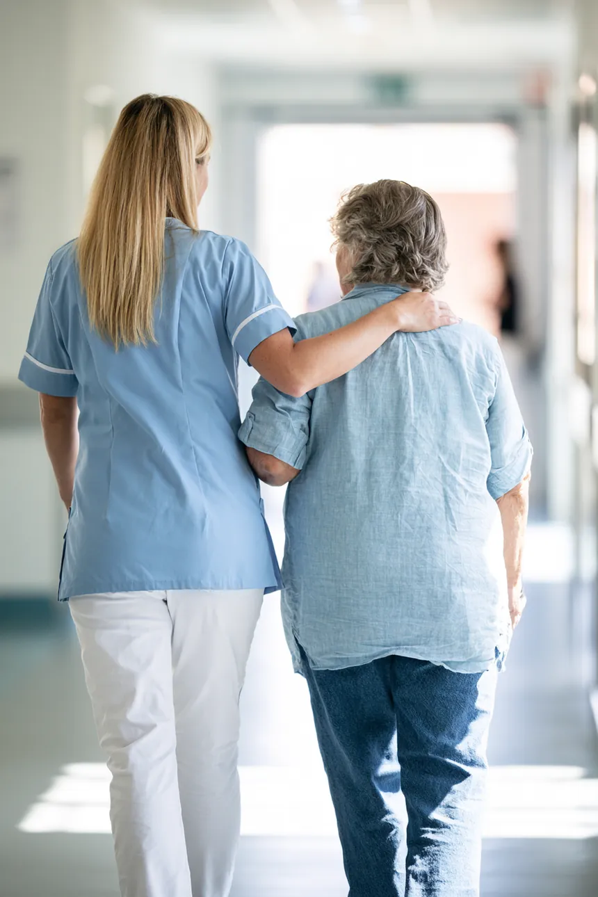 Nurse walking a patient toward the sunlit exit of a clinic corridor